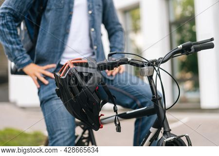Close-up Cropped Shot Of Bicycle Helmet Hanging On Handlebars Of Bike Standing In City Street Summer
