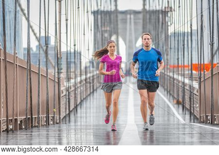 New York city runners athletes training for run marathon on Brooklyn Bridge. Fit active interracial couple on outdoor running exercise in raining day. Summer rain. Asian woman, Caucasian man.