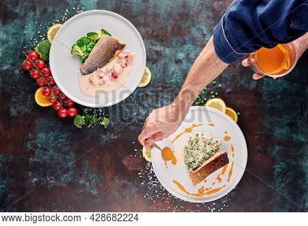 Chef Cook Grilled Salmon Steak And Sea Bass Steak With Vegetables On White Plates On A Blue Textured