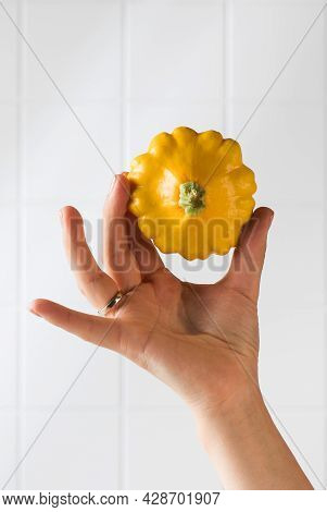 A Womans Hand Holds A Yellow Pattison On A White Tiled Background. Copy Space.