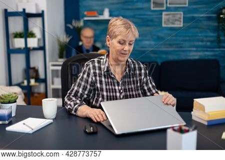 Mature Entrepreneur Sitting In Front Of Portable Computer In Office. Elderly Woman In Home Living Ro
