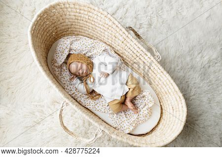 A Reborn Newborn Baby Doll Toy Dressed In A Mustard Colored Bonnet Hat And A White Cardigan Lying In