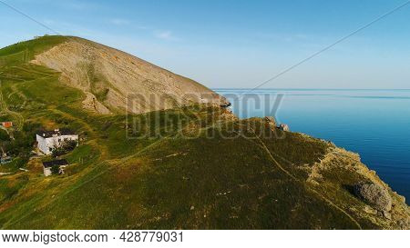 Top View Of Rocky Cape On Background Of Blue Sea. Shot. Remote Life In House On Sea Cape. Beautiful 