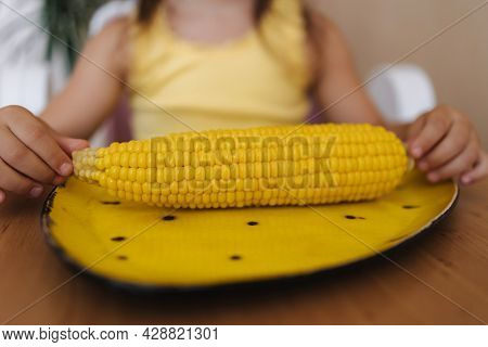 Close Up Of Little Girl Hold Corn In Hand. Fresh Corn On Yellow Plate