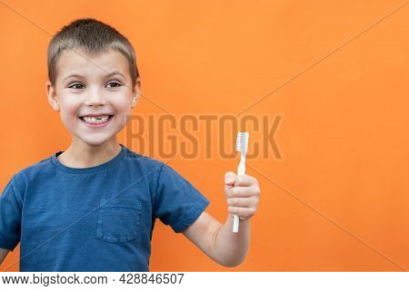 Boy Without Milk Upper Tooth In Blue T-shirt Smiles And Holds Toothbrush In Hand On The Orange Backg