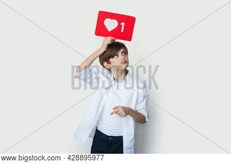 Cute Boy Is Holding A Paper With Like Sign Above The Head Posing On A White Studio Wall
