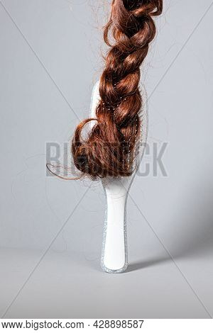 The Concept Of Hair Problems And Hair Care. A White Comb With A False Braid Of Hair Attached To It. 