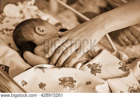 Mother Hands Are Stroking A Newborn Baby With A Maternity Hospital Bracelet On Her Arm. A Newly Born