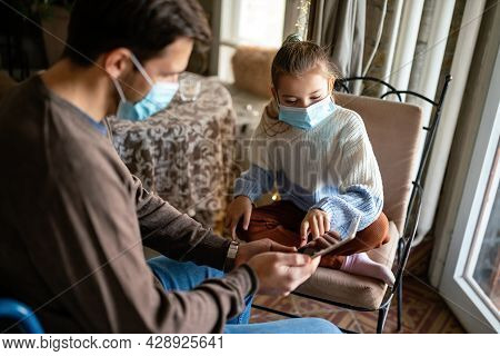 Father With Disability In Wheelchair Using Tablet At Home With Child While Wearing Masks.