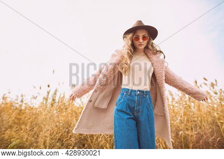 Attractive young woman in trendy autumn clothes poses in motion against the backdrop of an autumn landscape. Autumn fashion.