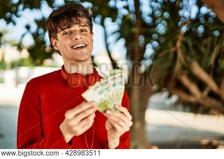 Young hispanic man using headphones counting argentinian pesos at the city
