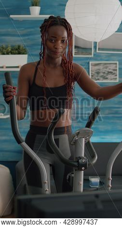 Black Woman Athletic Training On Elliptical Bike Practicing Cardio Sport Watching Aerobic Video On T