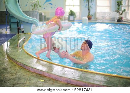 Little girl jumping with an inflatable round tube in the pool, her father in pool catches her