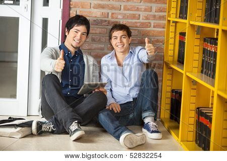 Full length portrait of multiethnic friends with digital tablet gesturing thumbsup while sitting in college library