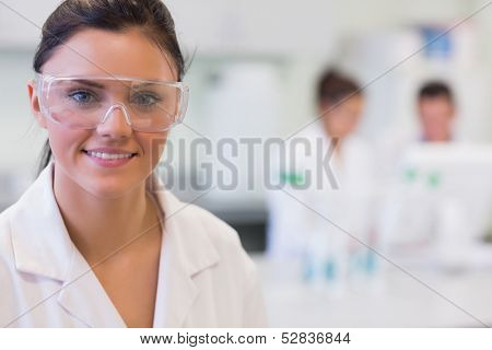Close-up portrait of a female researcher with colleagues in the background at laboratory