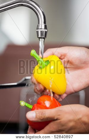 Kitchen porter washing red and yellow pepper under running tap in professional kitchen
