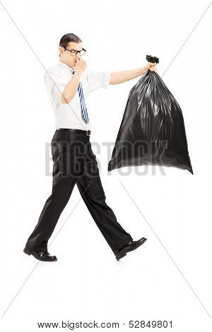 Full length portrait of a male closing his nose and carrying a stinky garbage bag isolated on white background