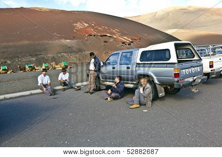 Camel Riders Wait For Tourists Being Guided By Local People Through The Famous Timanfaya National Pa