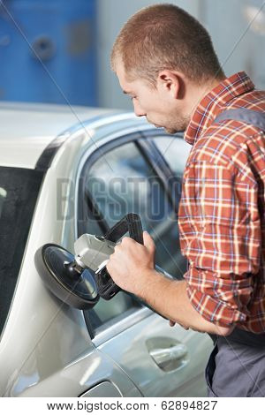 auto mechanic worker polishing car body at automobile repair and renew service station shop by power buffer machine