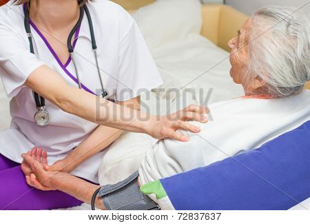 Young Nurse Caregiving An Old Lady Lying In Bed