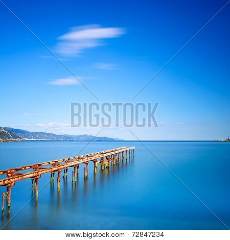 Wooden Pier Or Jetty Remains On A Blue Ocean Lake. Long Exposure.