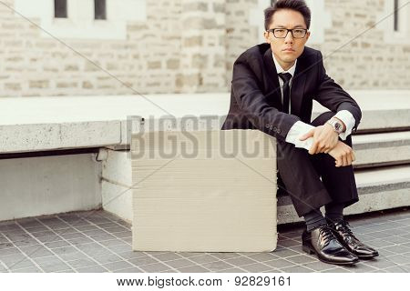 Businessman in a city street sitting next to blank banner