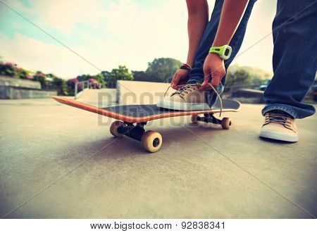 skateboarder hands tying shoelace at skatepark