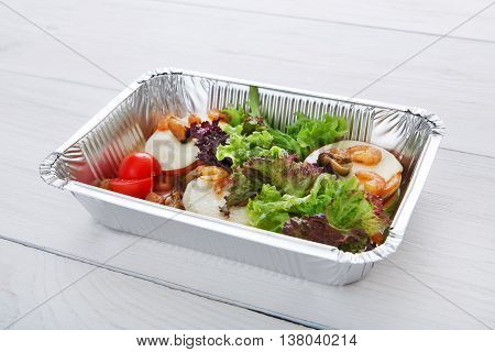 Healthy food and diet concept. Take away of fitness meal. Weight loss nutrition in foil boxes. Vegetables, lettuce and mozarella cheese with cherry tomatoes and shrimps at white wood