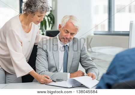 Senior manager helping senior employee complete the report. Team of businessman and businesswoman working on a business documet. Senior partners working together reviewing contract at office.
