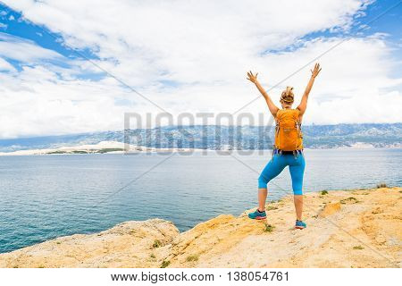 Woman hiker hiking with backpack arms outstretched looking at sea and mountains view. Accomplished climber with hands up outdoors. Beautiful inspirational landscape. Trekking and activity concept.