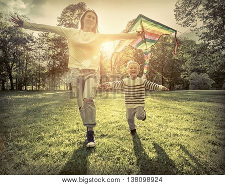 Runnings little boy and mother flies with them kite in the park under sunligt.