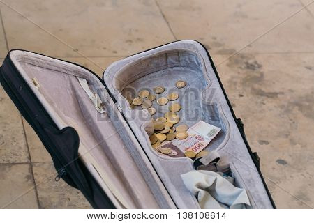 Violin case with paper money and coins on street pavement background