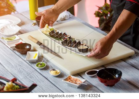 Hands hold plate with sushi. Sushi rolls on long plate. Futomaki rolls served at restaurant. Finest dish from the menu.