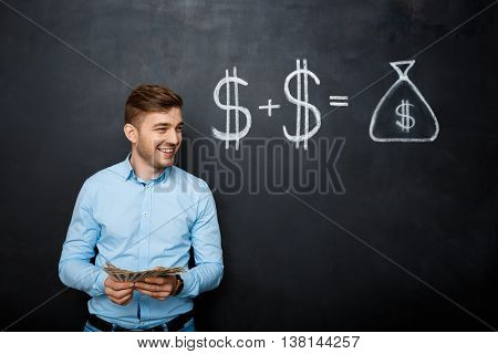 handsome man standing over blackboard. Holding dollars in his hands and smiling