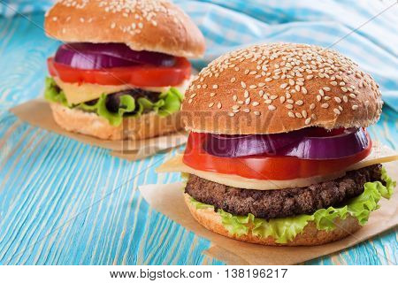 Two homemade cheeseburgers with beef patties and fresh salad on seasame buns, sered on blue wooden table.