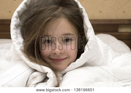 portrait of posing Caucasian brunette young girl of 7 - 8 years old laying in bed covered with white blanket over her head