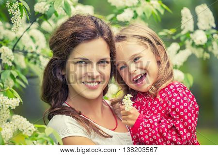 Outdoor portrait of happy mother and daughter in bloomimg flowers