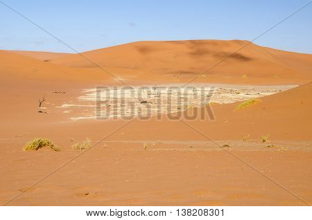 Dunes of Sossusvlei or Deadvlei with a fragment of a clay pan and skeletons of old dead trees in Namib desert Namibia.