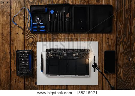 Top view on cleaned and repaired laptop computer isolated on vintage wooden table near professional tools and smartphone before assembling back