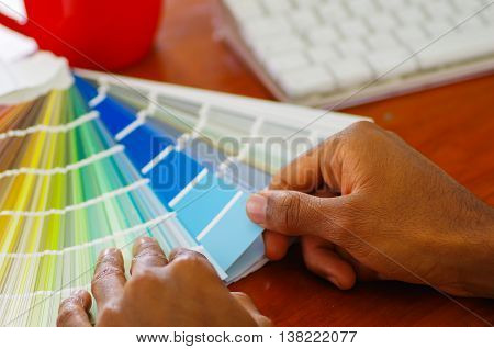 Closeup hands holding palette, colormap spread out in front of white computer keyboard, designer concept.