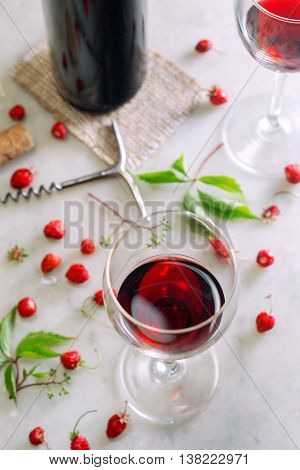 Glasses of red wine on the marble table with fresh strawberries. Shallow DOF