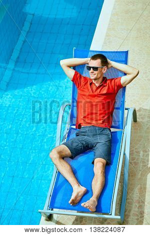 young man relaxing on the chaise-longue near the pool. man wearing in red polo shirt and sunglass
