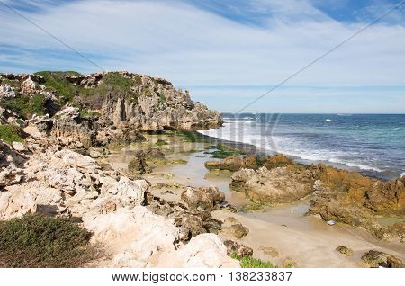 Rugged limestone cliffs and rocky beach under a blue sky with clouds at Penguin Island in Rockingham, Western Australia.