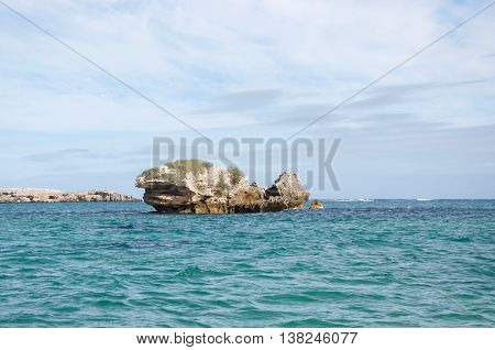 Limestone rock formations with in the turquoise Indian Ocean waters with Penguin Island in the background under a cloudy sky in Rockingham, Western Australia.