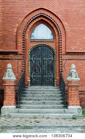 Massive wooden church door with a handle forged with an iron grip settled into a brick wall at the church. Breclav. South Moravia
