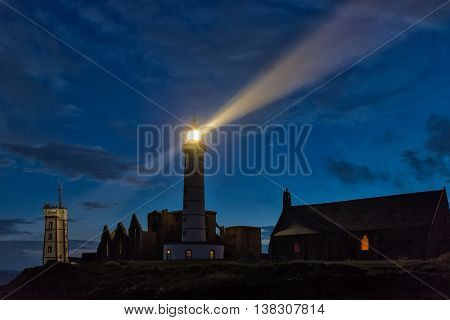 Mystical church and lighthouse illuminated over cloudy sky at Saint Mathieu point, Brittany, France