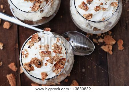 Three glasses of crumbled chocolate chip cookies and cheesecake parfaits against a rustic background. Extreme shallow depth of field with selective focus on top of desserts.