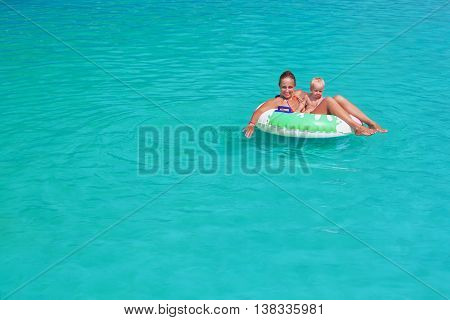 Funny happy family in turquoise beach pool - mother baby son swim sunbathing with fun. Healthy lifestyle active parent people water sports activity and swimming lesson on summer holiday with child
