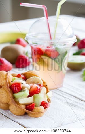 waffles with fruits strawberries apple and kiwi and lemonade on the wooden table