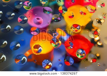 Bright colorful abstract background - view through glass with drops of water on a blurry bailers and buckets. Selective focus on foreground.